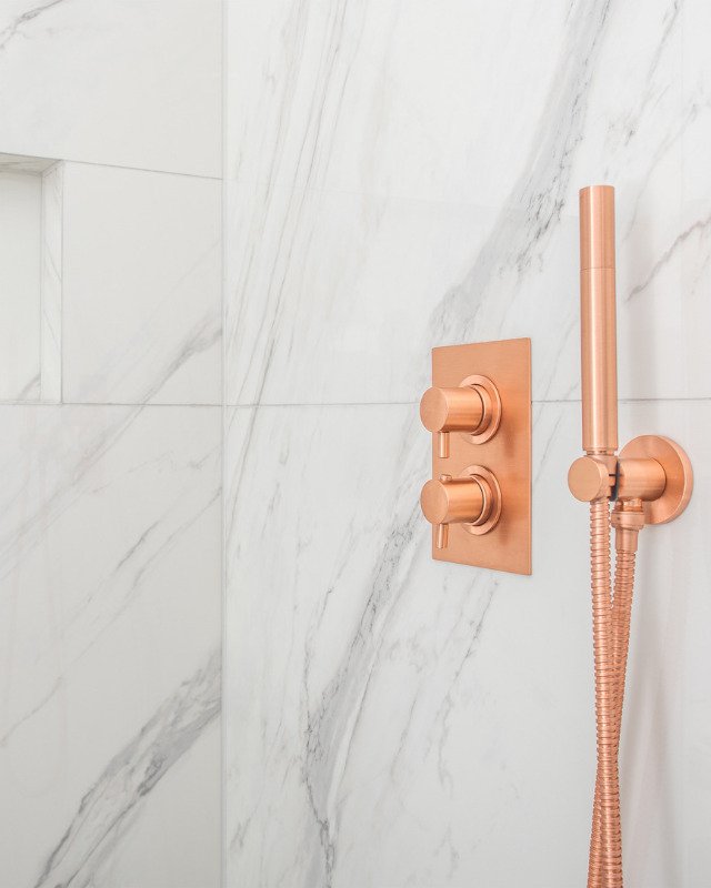 Image of a beautiful bath remodel with Copper Metallic Shower Water Control Valves and white and gray large marble tile.
