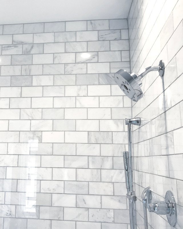 Image of an elegant bath remodel in Brick Town, NJ. Image showcases a shower with white and gray marble with a silver showerhead.