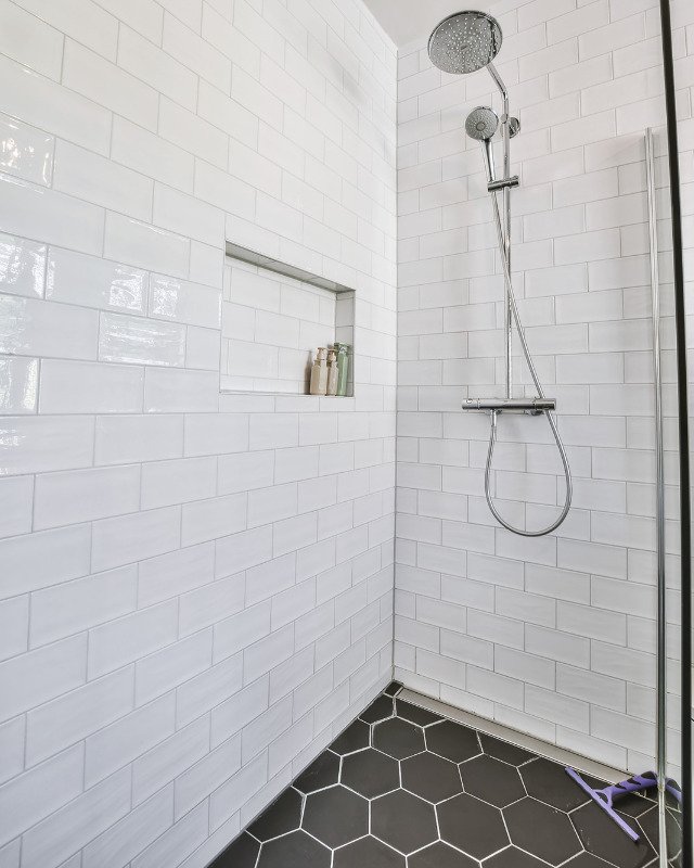 An image of a bath remodel in Lakewood, NJ highlighting a shower with white subway tiles and a black hexagon pattern tile floor.