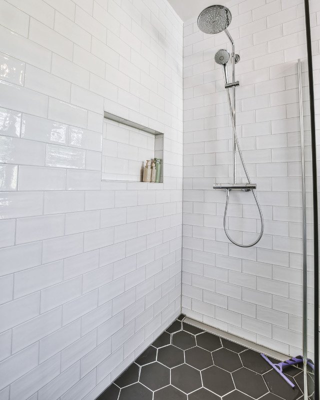 An image of a bath remodel in Toms River, NJ highlighting a shower with white subway tiles and a black hexagon pattern tile floor.